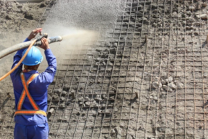 A man spraying shotcrete on a building wall using a shotcrete machine