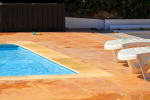 A pool deck with a clean blue pool, an umbrella, and relaxing chairs that have been recently repaired