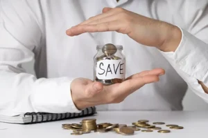 A man cupping a glass jar filled with coins labeled “save”