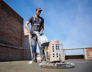 A man in overalls sealing the concrete on a rooftop