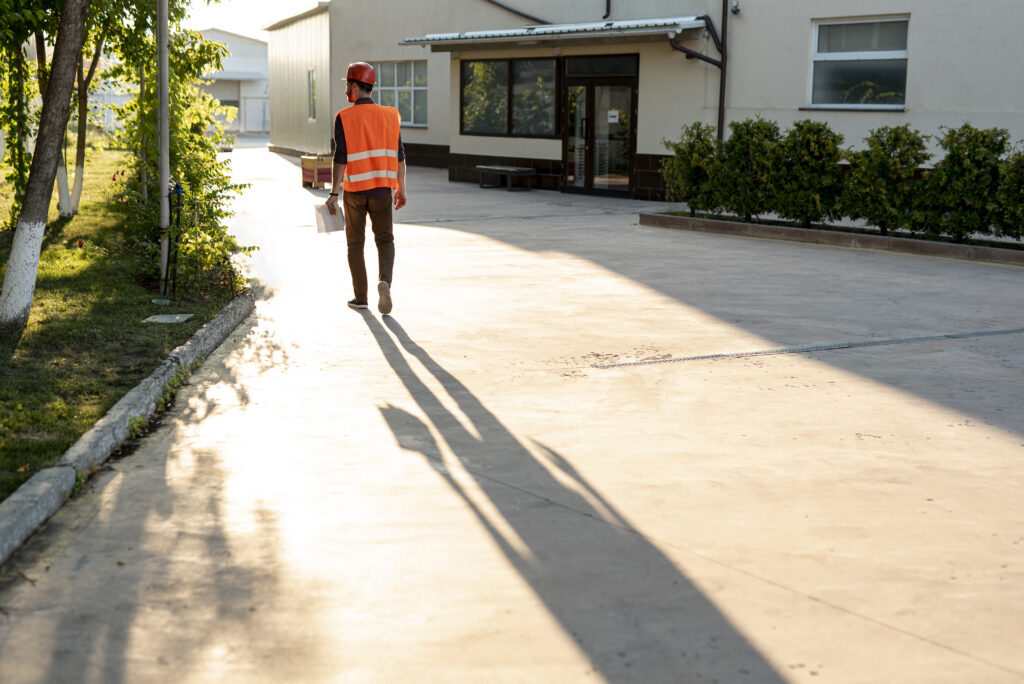 A construction worker in a reflective vest and hard hat walking down a concrete driveway in a home in Long Island