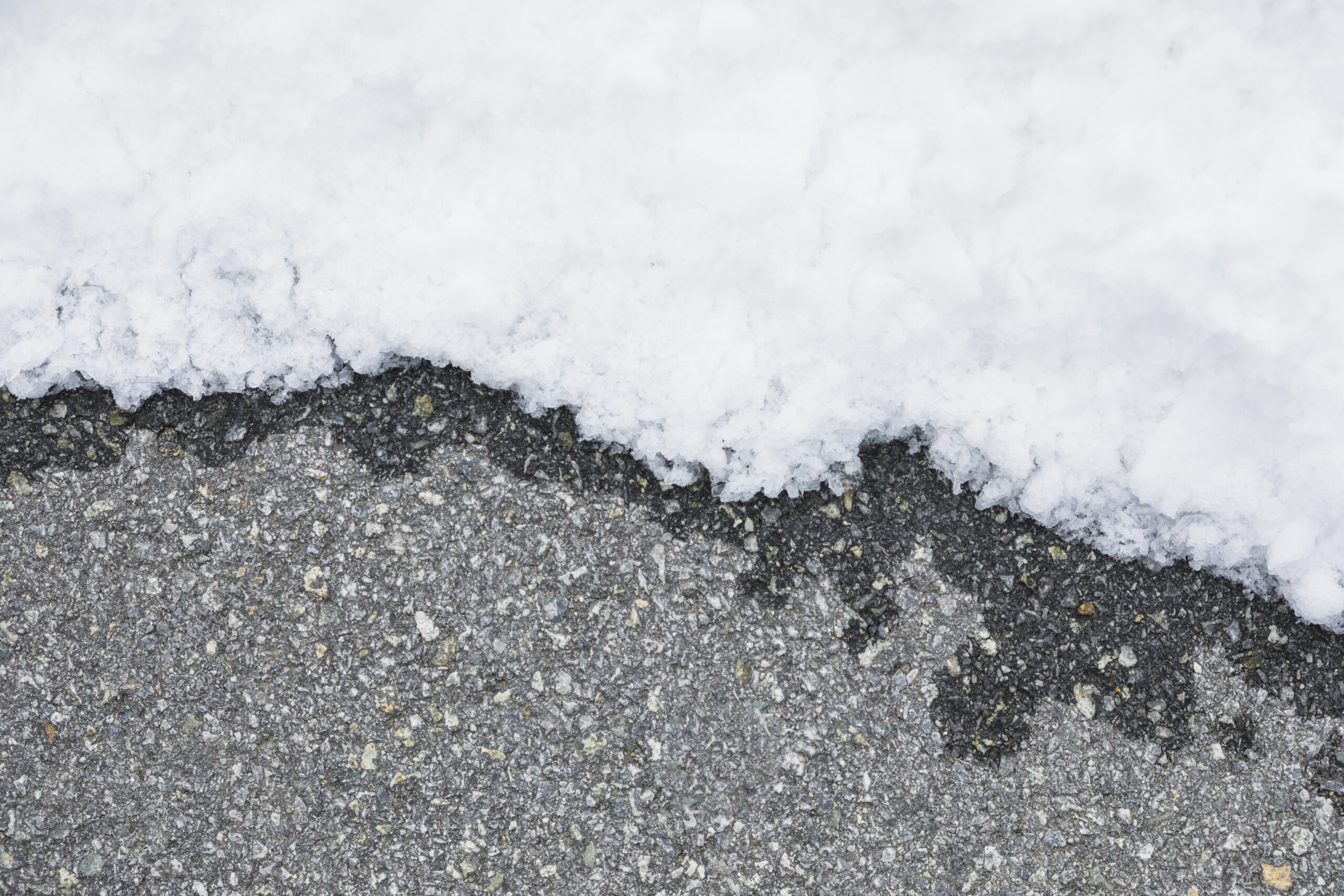 A concrete surface that is half covered with snow.