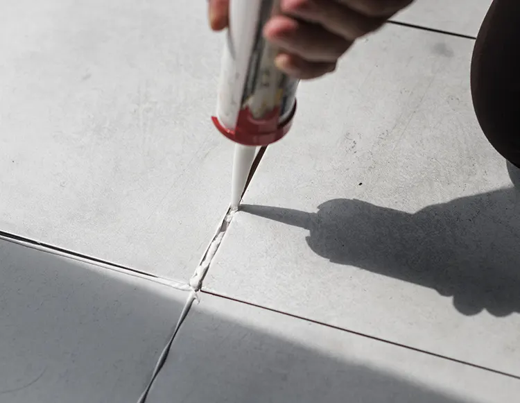 A contractor holding a big caulking gun and applying it between concrete slabs.