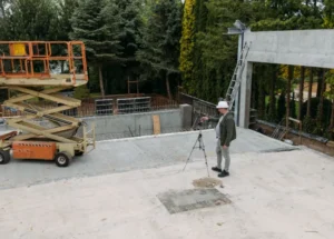 Concrete Patio Cracked and Unlevel - A Contractor Standing on a Cracked Commercial Patio with Surveying Equipment