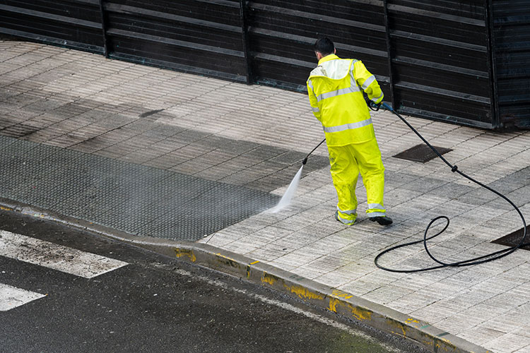 A contractor in reflective overalls pressure washing a sidewalk in NYC.