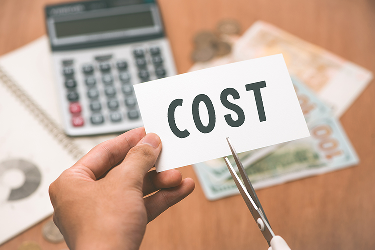 A man holding a label with the word, “COST” on it over a study table with books and a calculator.