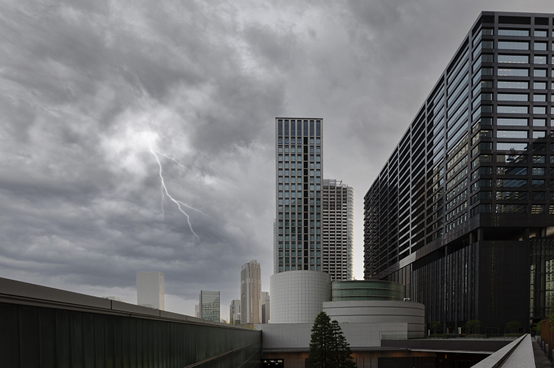 A city skiline with a lightning bolt in the sky and heavy grey clouds